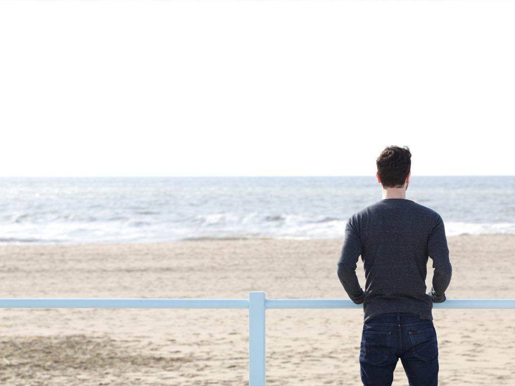 A man standing on the beach looking out over the water.