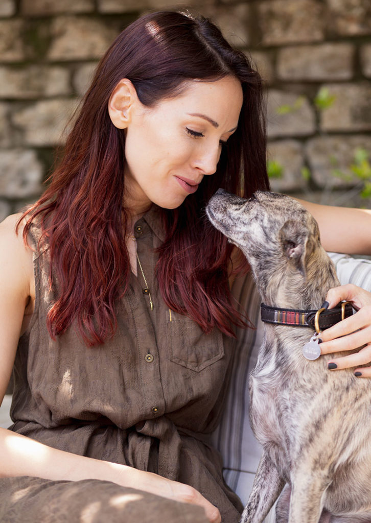 A woman holding her dog and kissing it.