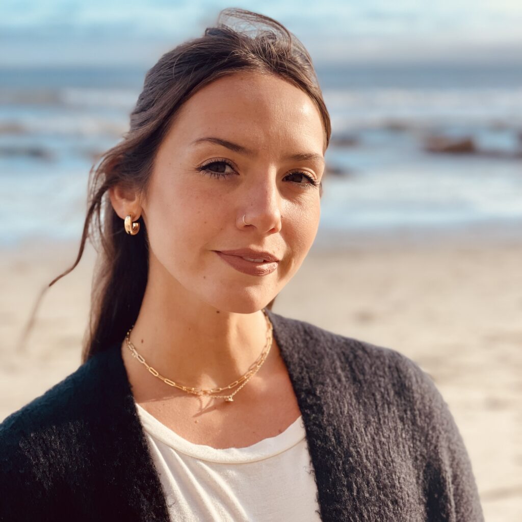 A woman standing on the beach wearing a black jacket.